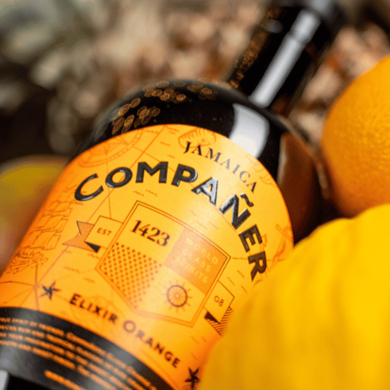 Companero Ron Elixir Orange Moodbild - Flasche liegt neben einigen Orangen