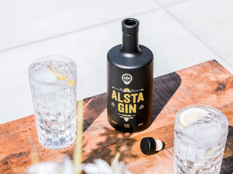 Alsta Gin Moodbild -geöffnete Flasche steht auf einem Tisch, daneben zwei Gläser