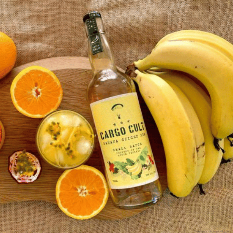 Cargo Cult Rum Moodbild - Bananspiced liegt neben Banenen und Orangen auf einem Tuch