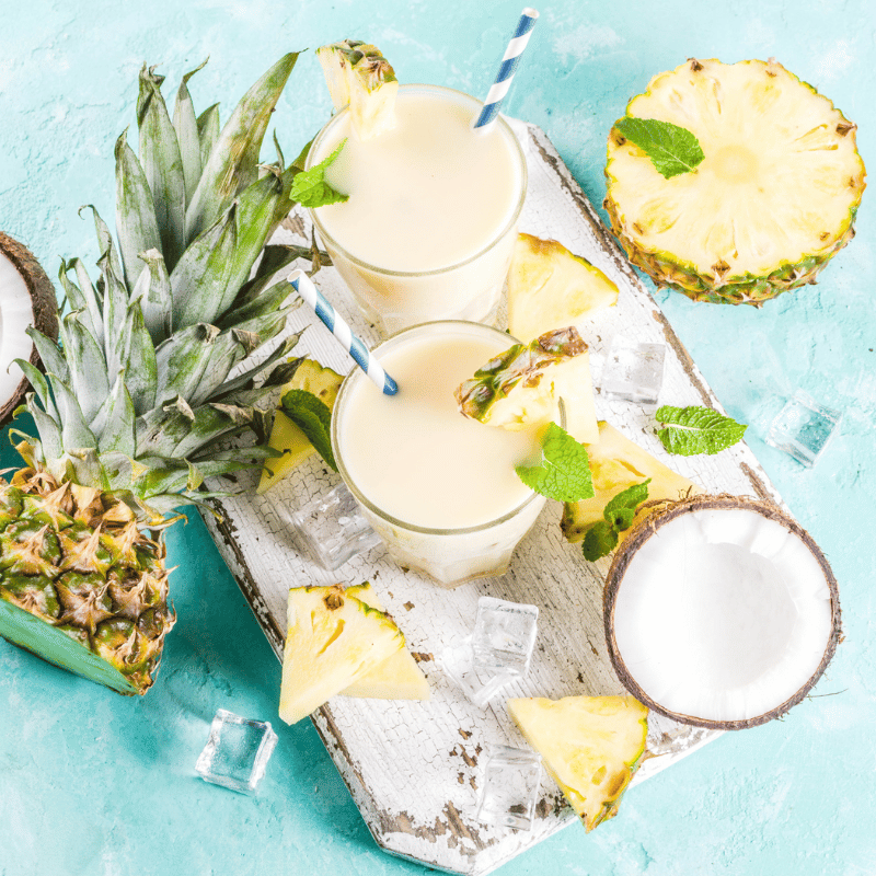 Colada Cocktail Moodbild - Zwei Cocktails stehen auf einem Brett zwischen Kokosnuss und Ananas