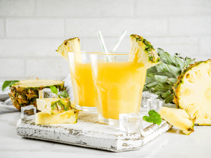 Colada Cocktail Moodbild - Zwei Gläser mit Colada, drum herum Eiswürfel und Ananas