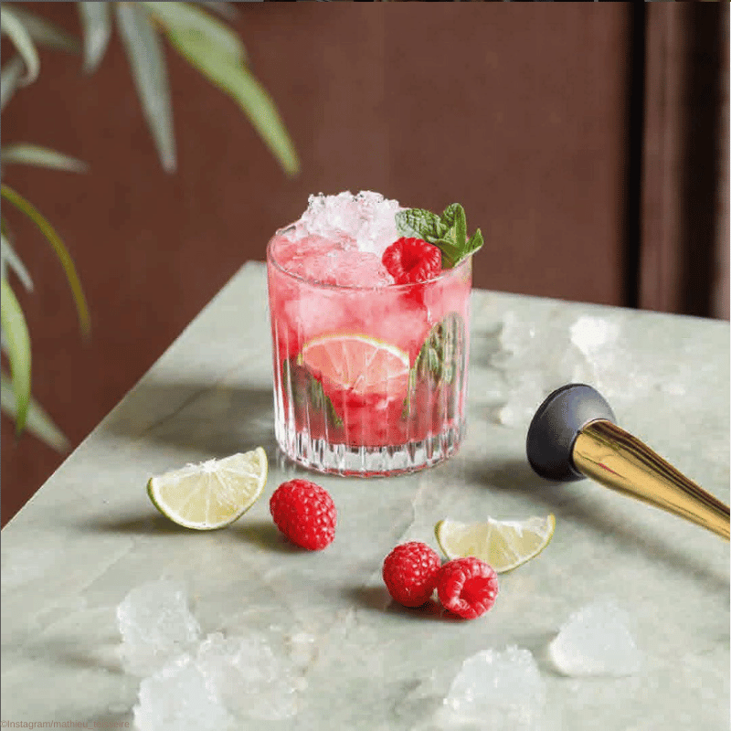 Mathieu Teisseire Moodbild - Ein Cocktailglas mit Eis und Früchten steht auf einem Tisch, daneben liegt ein Mörsel