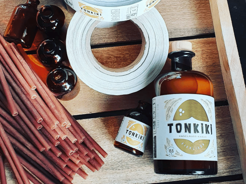 Tonkiki Eierlikoer Moodbild - Eine große und eine kleinere Flasche liegen auf einer Holkiste danben leere Flaschen und Etiketten
