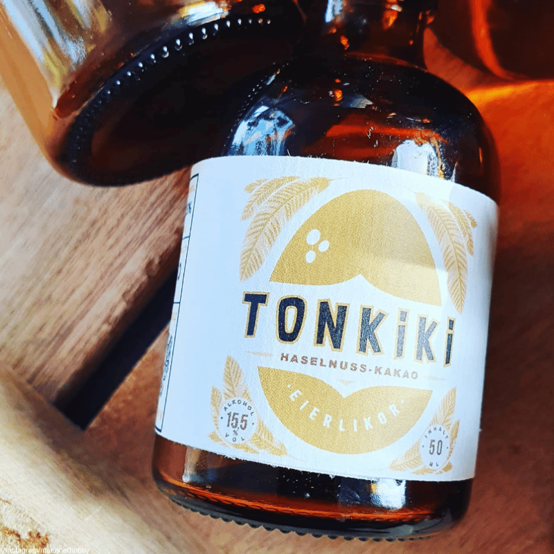Tonkiki Eierlikör Moodbild - Flasche liegt mit dem Ruecken auf einem Holzboden, darüber sind ncoh mehr flaschen zu sehen
