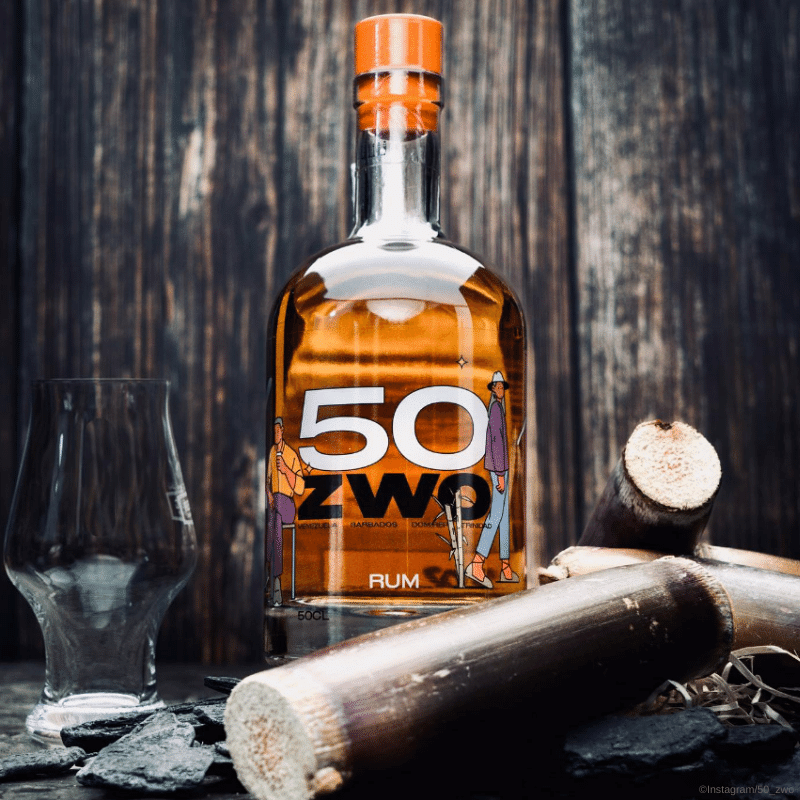 50ZWO Moodbild - 50ZWO Rum steht neben einem Glas und zwischen einigen Holzstücken. Dahinter ist eine Holzwand